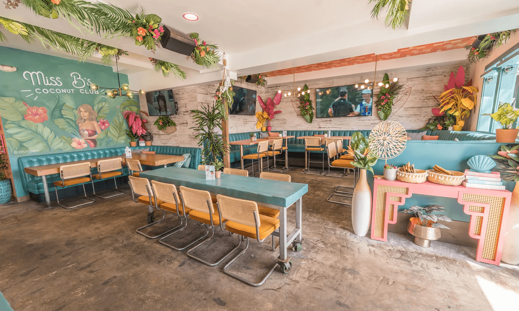 Miss B's Coconut Club dining room with teal tables, tropical murals, and open-air windows