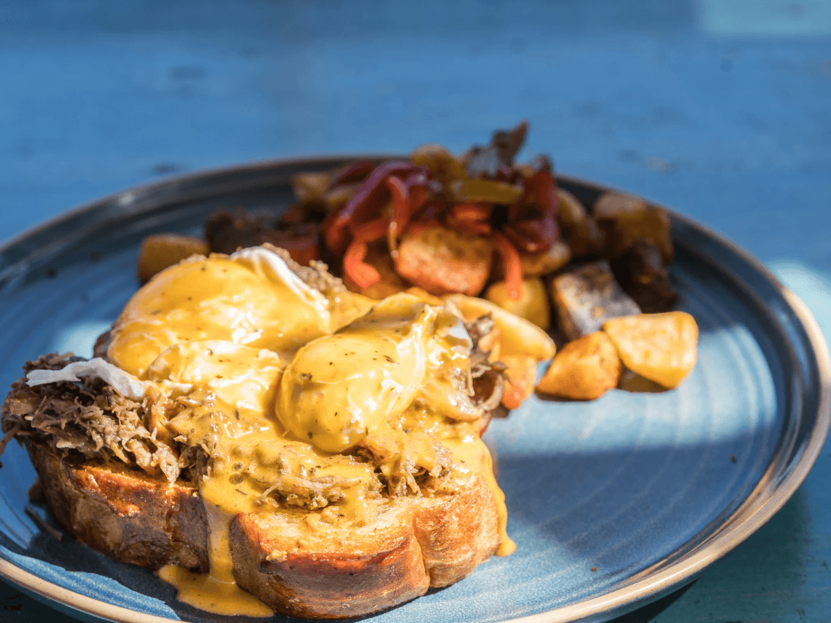 Eggs Benedict with hollandaise and breakfast potatoes on a blue plate at Miss B's Coconut Club